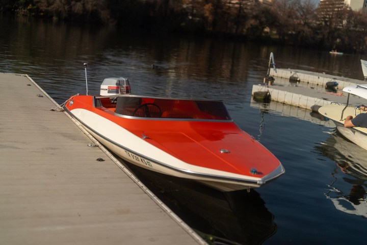 Red and white speedboat docked on calm water near a wooden pier.