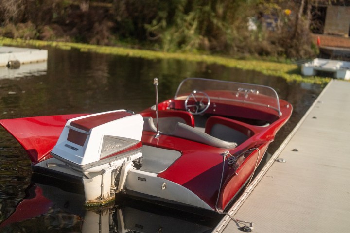 Red vintage speedboat moored at a wooden dock on a calm lake.