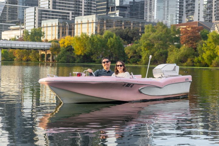 Couple on a pink boat in a river with city skyscrapers in the background.