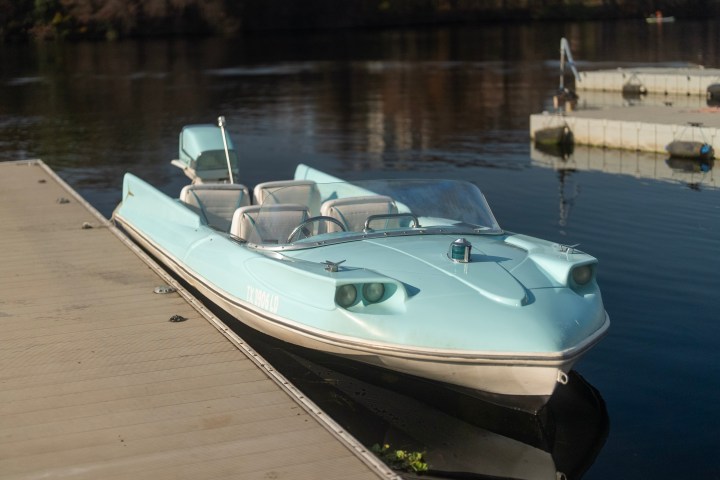 A light blue retro-style motorboat docked on a wooden pier by calm water.