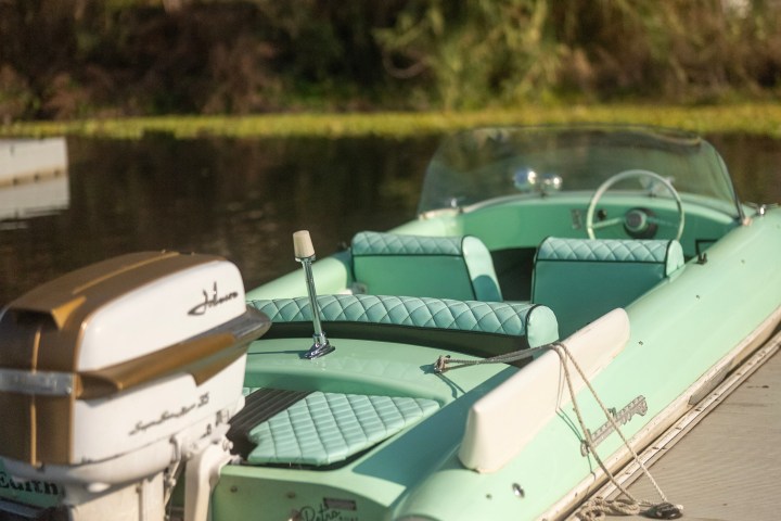 Vintage mint-green boat with outboard motor docked on a calm lake.