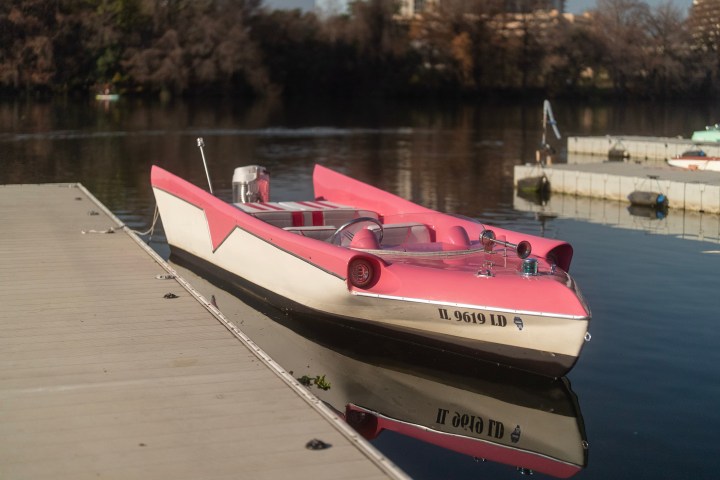 Pink and white retro speedboat moored at a dock on a calm lake.