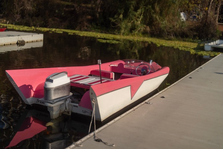 Pink vintage boat with an outboard engine docked on calm water.