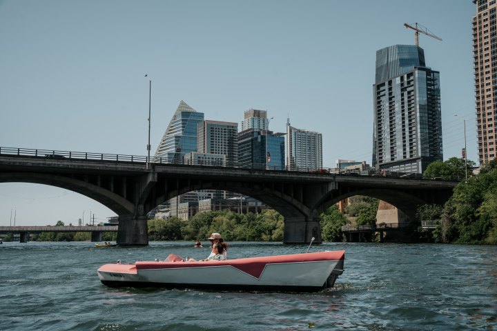 Person in a small boat on a river with a cityscape and bridge in the background.