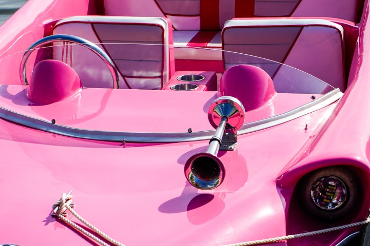 Pink vintage boat with striped seats moored on water.