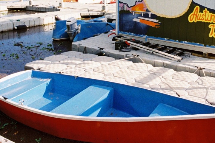 Red and blue boat docked near platform with Austin, TX mural.