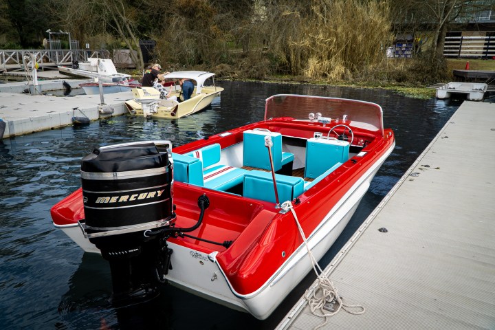 Red and white boat with turquoise seats docked beside a pier.