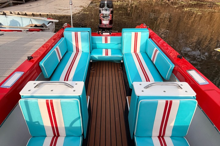 Colorful boat interior with blue and red-striped seats docked by a wooden deck.