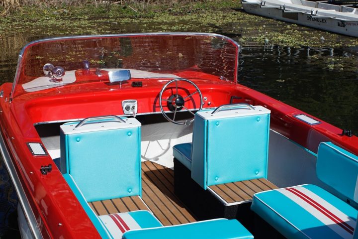 Red and teal vintage speedboat with teal seats docked near a building.